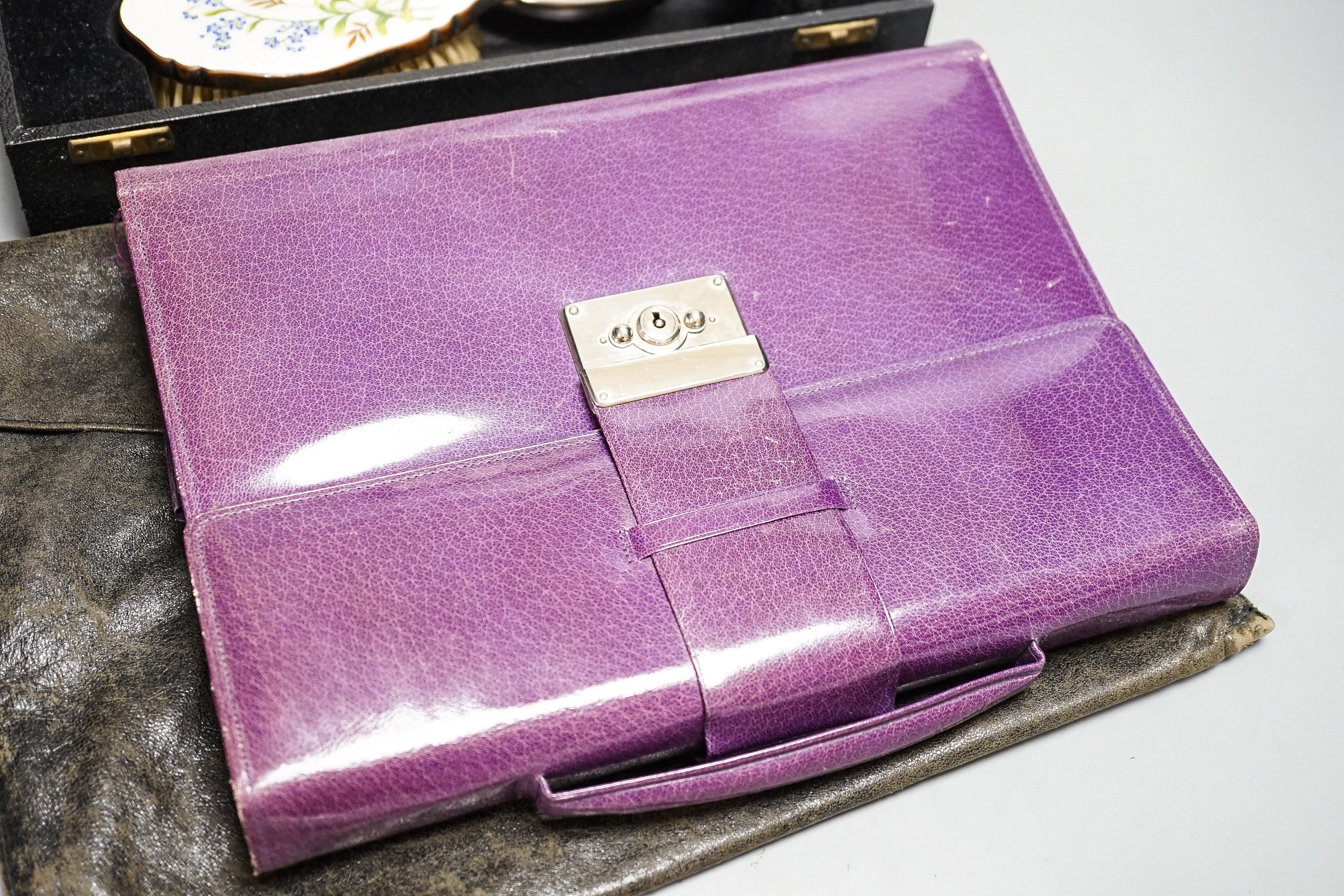 A boxed, three piece silver plated translucent enamelled dressing set, a purple leather stationary case and an evening bag